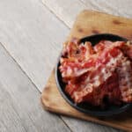 piatto con fette di pancetta su tavolo in legno