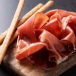 fette di prosciutto crudo toscano con grissini su tagliere in legno