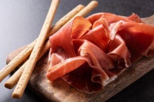 fette di prosciutto crudo toscano con grissini su tagliere in legno