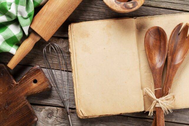 libro di ricette con utensili da cucina su tavolo in legno